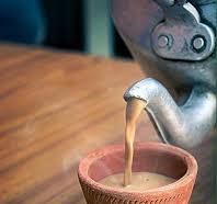 An image of chai being poured onto a mud cup from a metal kettle